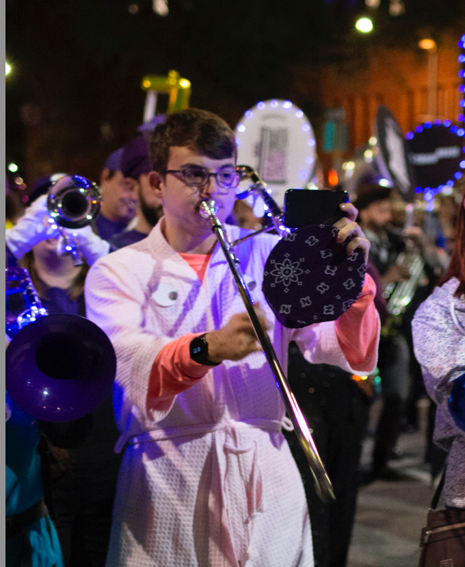 Trombone player in a Halloween costume playing while holding their phone in their hand